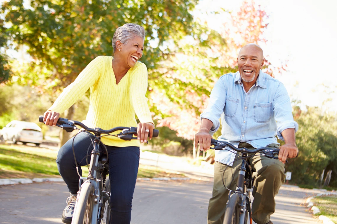 An older woman and man, both smiling, ride bikes side by side