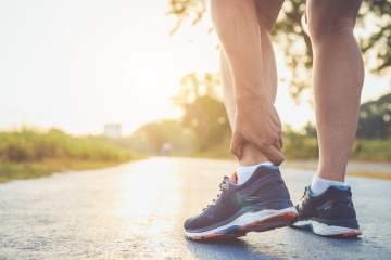 Runner reaching down to hold ankle on a sunlit path